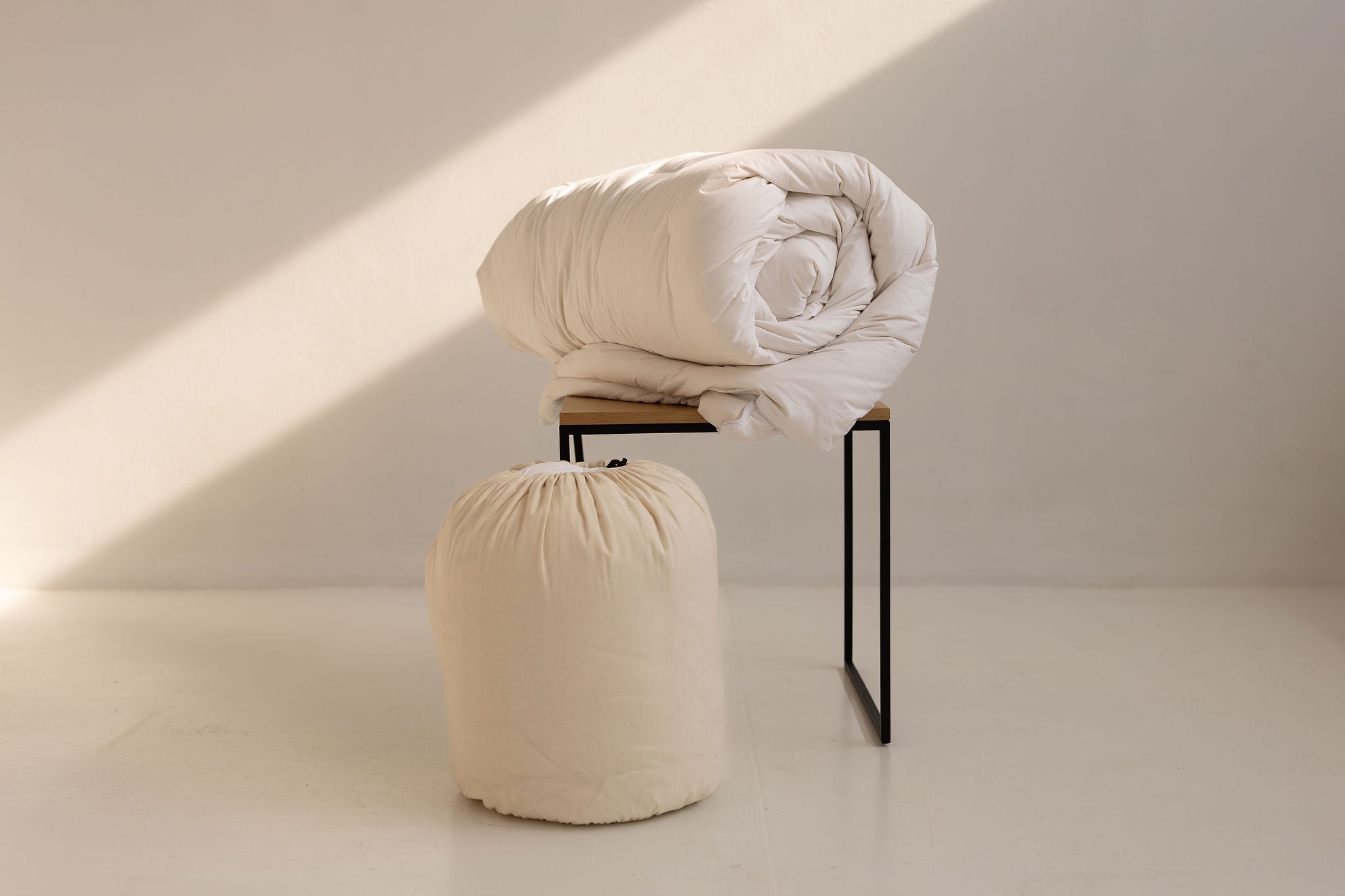 Folded white blanket on a small stool with a light beige background