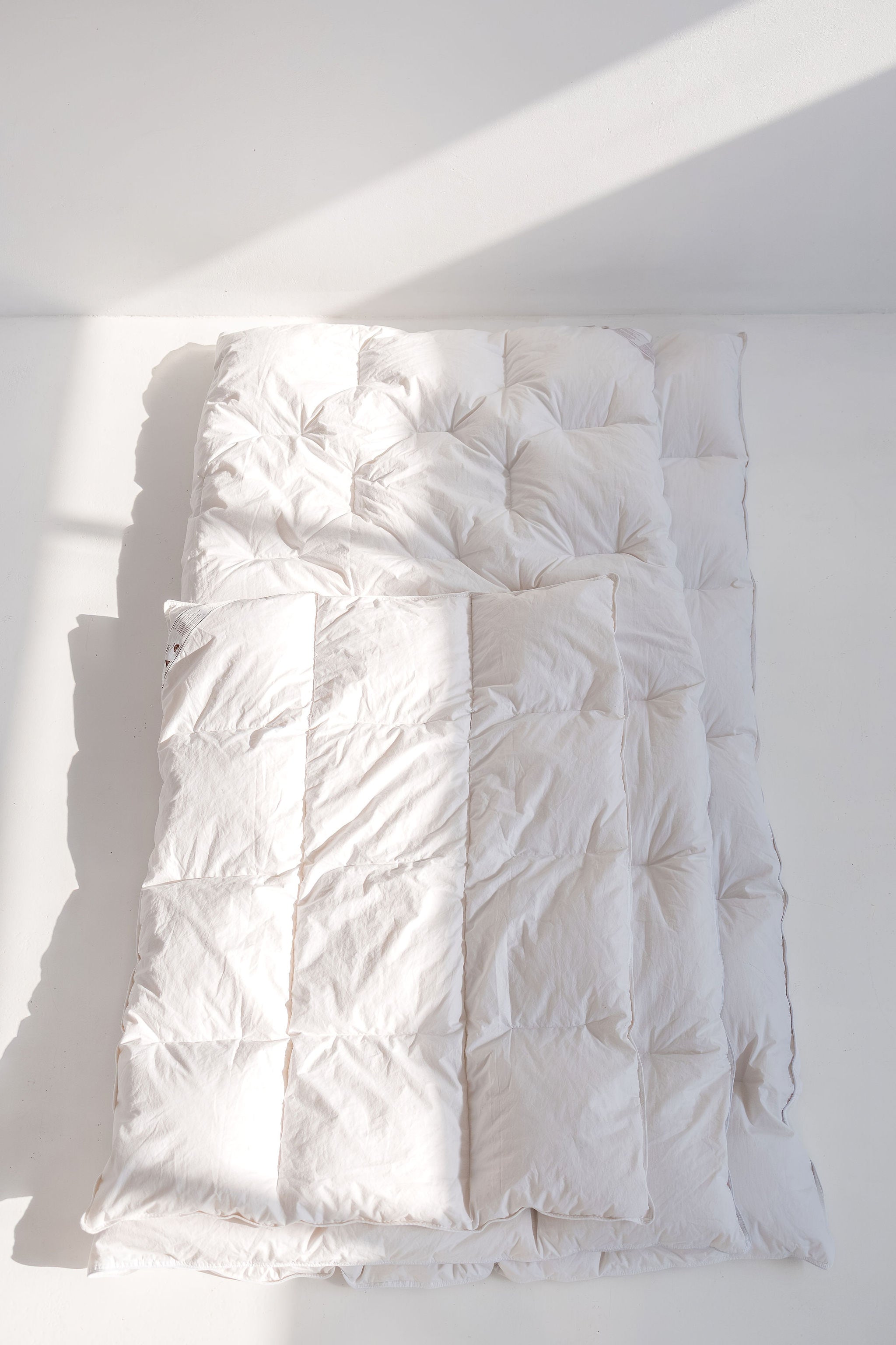 White quilted comforter on a bed with sunlight casting shadows