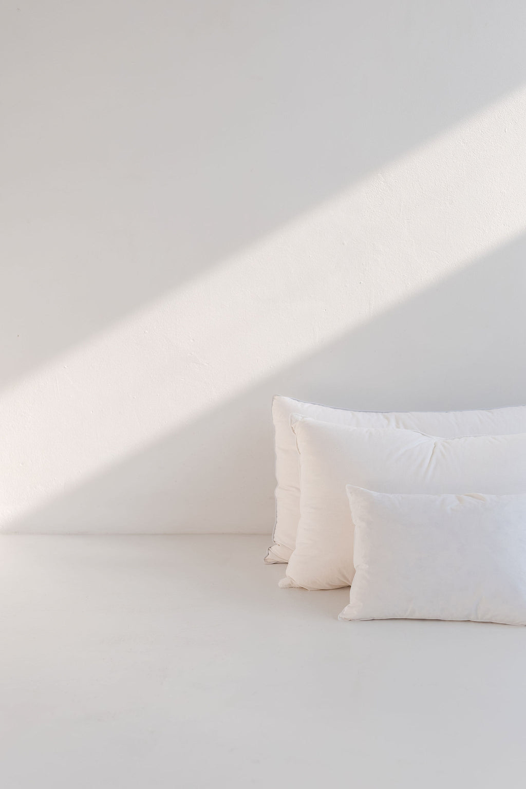 Three white pillows on a light gray surface with a soft shadow