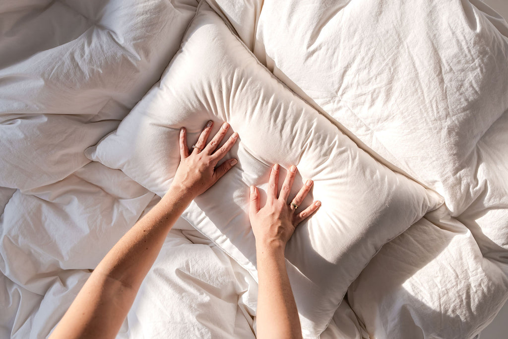 Person's hands touching a white pillow on a bed